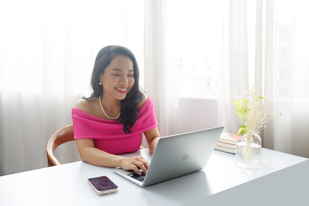 Elegant businesswoman in pink dress working at a desk indoors, smiling and focused.