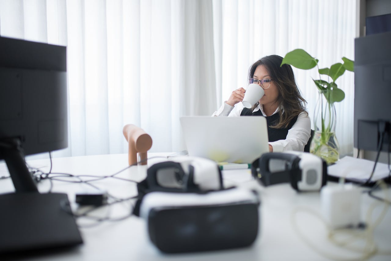 Businesswoman sips coffee while working on laptop in a contemporary office setting.
